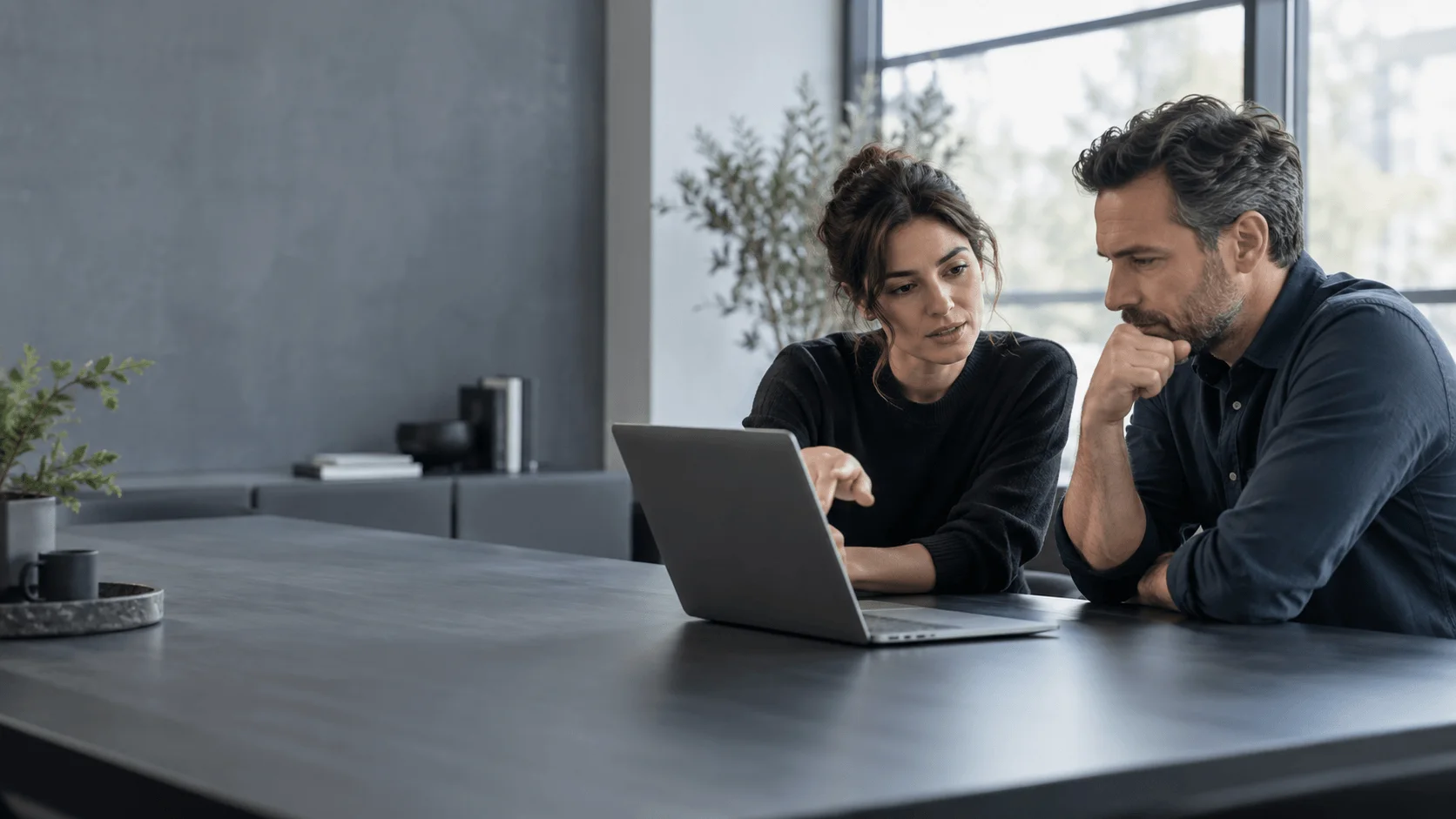Two colleagues reviewing software on a laptop at a dark meeting table